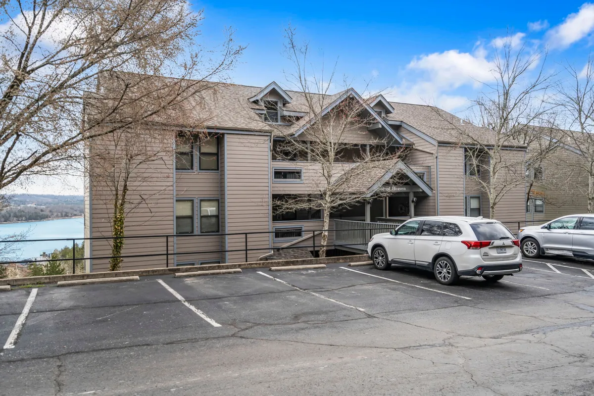 A serene exterior view of the building facade with parking area, flanked by mature trees, and a clear view of Table Rock Lake in the background. The image captures the surrounding natural beauty and the tranquil lakeside atmosphere.
