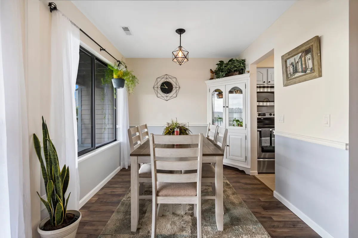 This image focuses on a charming dining area with a large table, a stylish hanging light fixture, and windows with potted plants nearby. The setup radiates warmth and is ideal for family dinners or quick breakfasts, as described in the section.