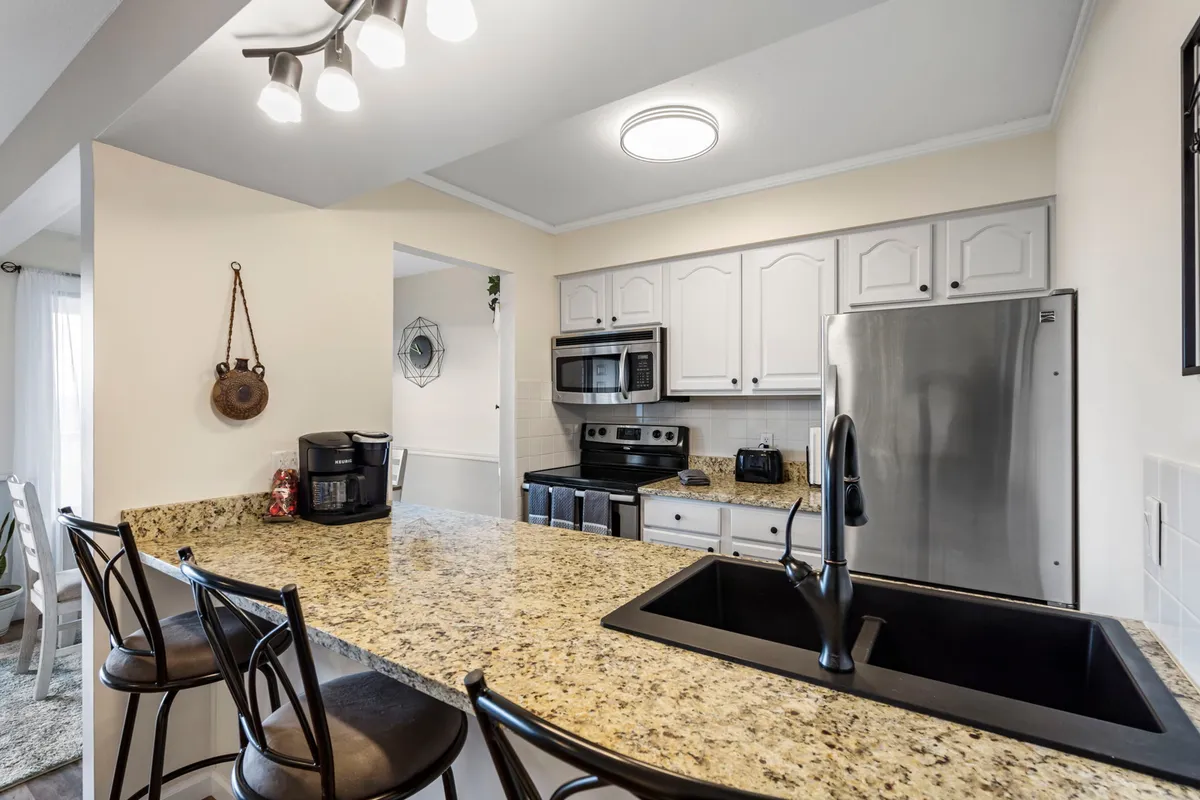 This image showcases a modern kitchen with beautiful granite countertops, stainless steel appliances, and a large kitchen island with seating. The space is well-lit and inviting, exuding warmth and functionality. Elements such as the visible dishwasher and oven reinforce the sense of a fully equipped, upgraded kitchen.