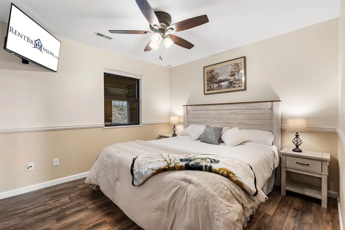 A spacious king-size bed with elegant decorative wall art above, a cozy nightstand with a lamp, and a wall-mounted television. Soft, inviting bedding and ambient lighting create a soothing atmosphere, perfect for restful sleep or relaxing with a show.