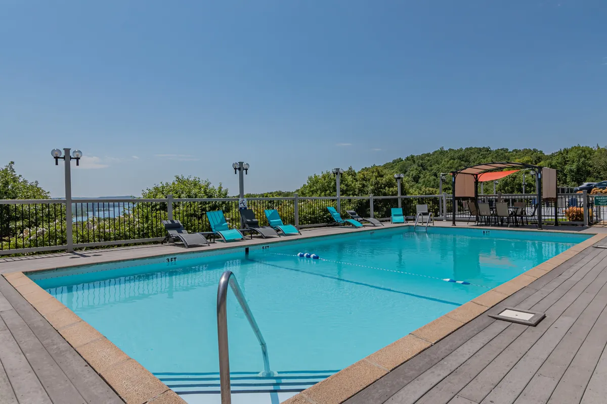 A bright, inviting outdoor pool area with sparkling water, ample lounge chairs, a canopy for shade, and lush greenery surrounding the space. The atmosphere evokes relaxation and resort-style leisure, perfect for summer enjoyment.
