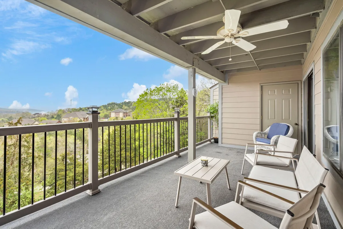 This image displays an inviting private deck with outdoor seating and a table, set against a backdrop of lush greenery. The view from the deck showcases the serene natural environment and hints at the lake beyond, presenting the ideal spot for morning coffee or evening toasts.